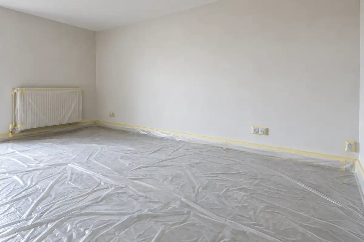 Sol, plinthes et radiateur sont protégés avant la peinture, tandis que le mur reste prêt à recevoir la pulvérisation.